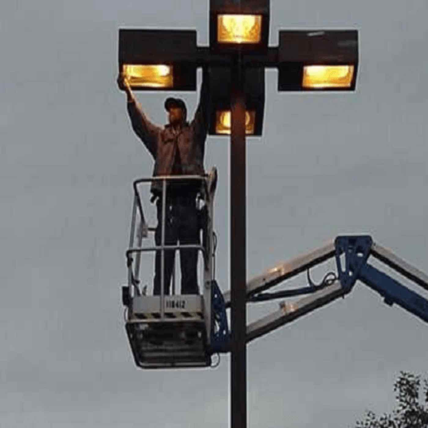 An electrician on a lift servicing parking lot lights.